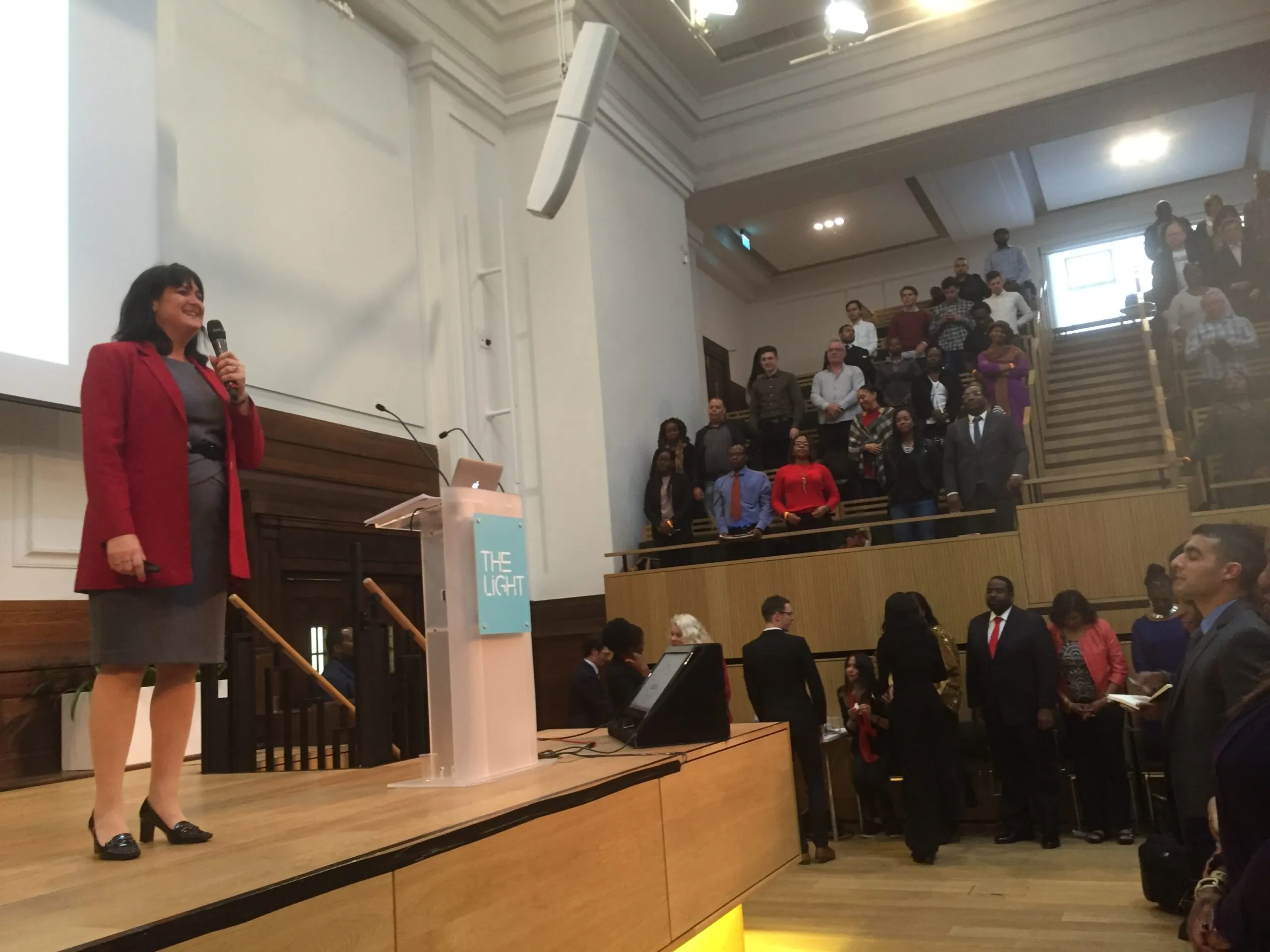 Mindy standing on a podium with a microphone in front of a crowd of people
